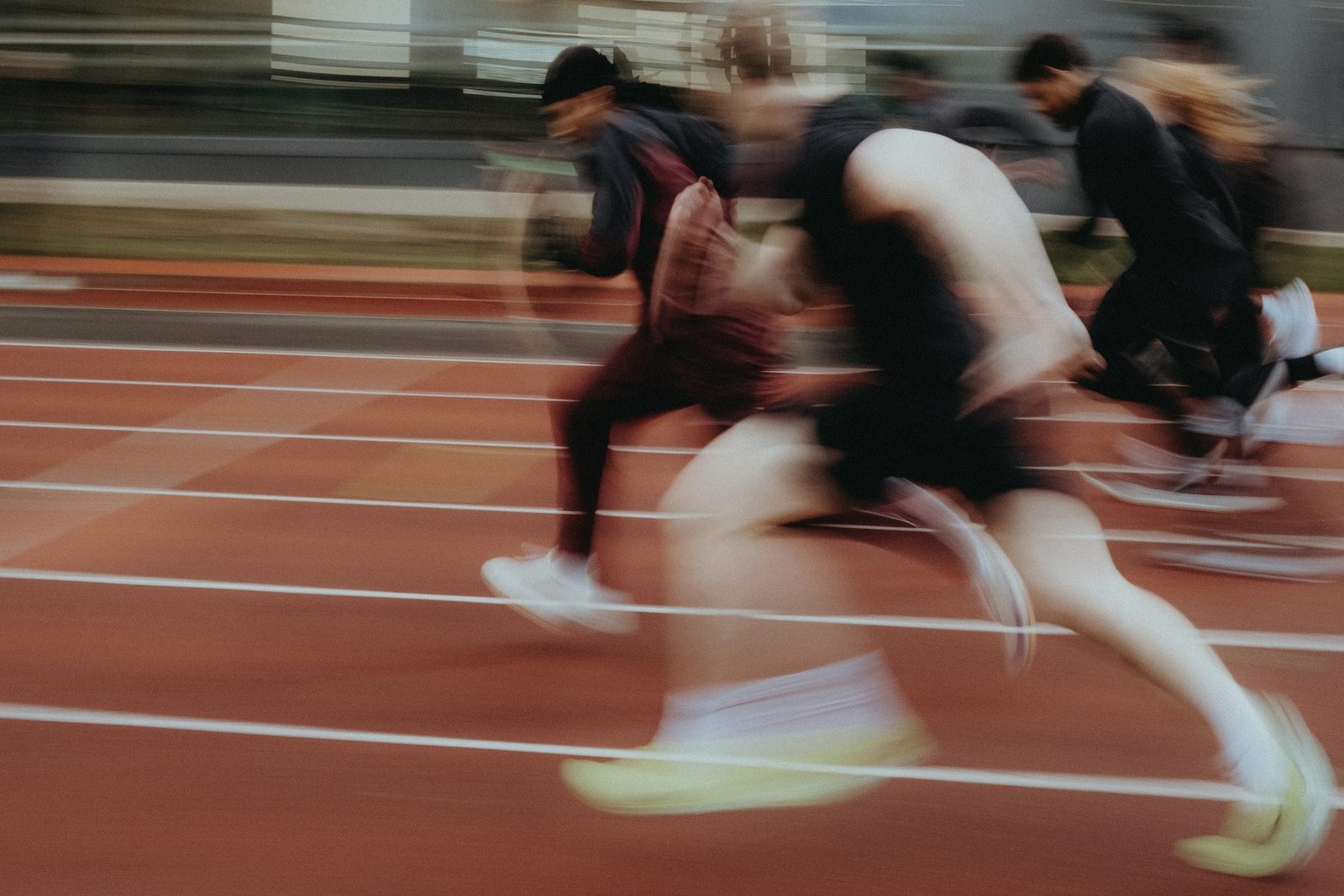 Sprinters at full stride down a floodlit track, motion-blurred